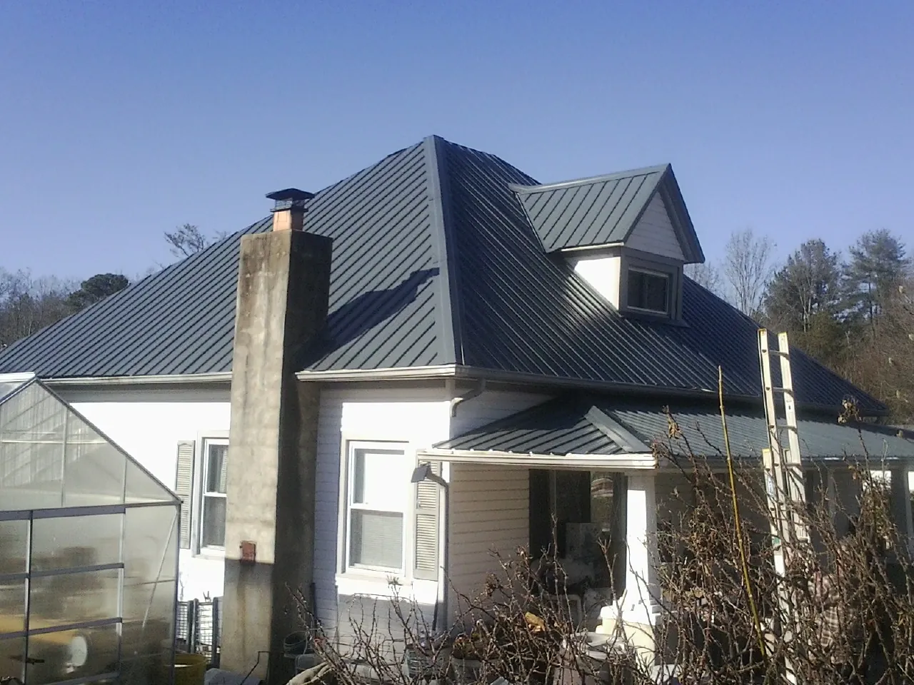 Dark blue standing seam metal roof on a white farmhouse with dormer — Slate & Tile Roof Repair by Roofing Brothers in Milton Center