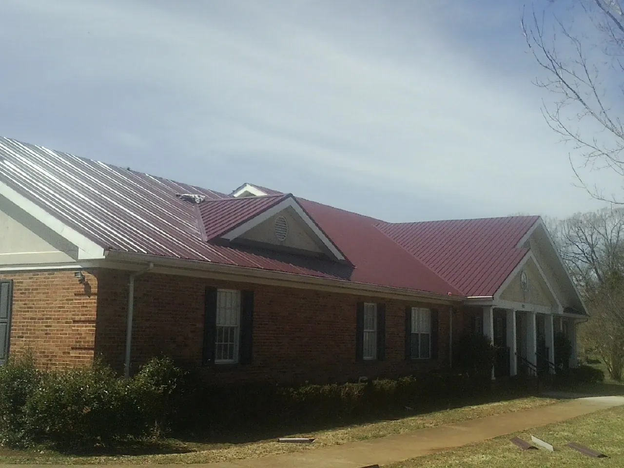Red metal roof with gabled entries on a long brick building, from a Hail Damage Roof Repair job in Milton Center
