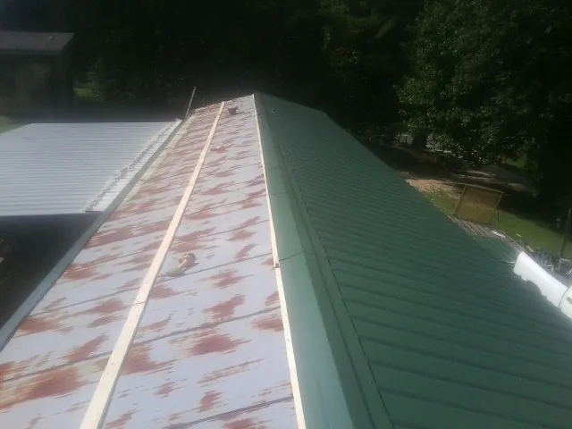 Old rusted panels beside newly installed green metal roofing — Wind Damage Roof Repair by Roofing Brothers in Milton Center