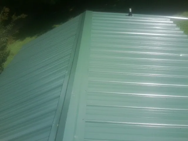 New green metal panels meeting at the ridge of a roof — Flat Roof Repair work by our crew in Milton Center