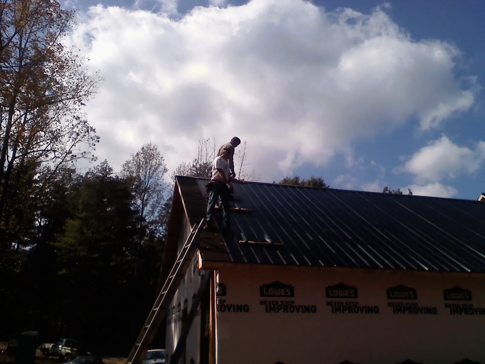 Roofer fastening dark metal panels high against a cloudy sky, from a Roof Inspection job in Milton Center