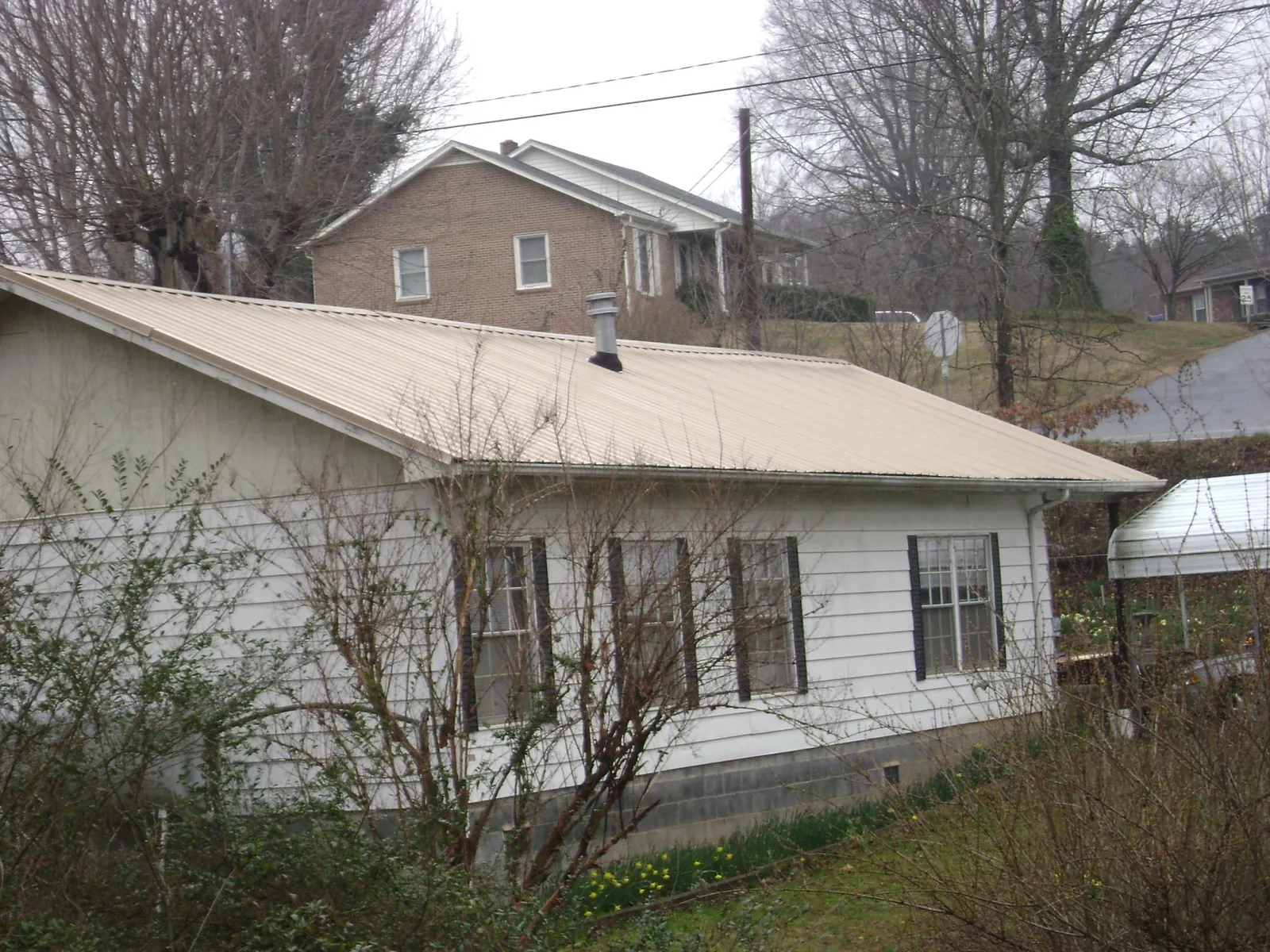 Tan metal roof on a white sided house set into a hillside — Commercial Roofing by Roofing Brothers in Milton Center