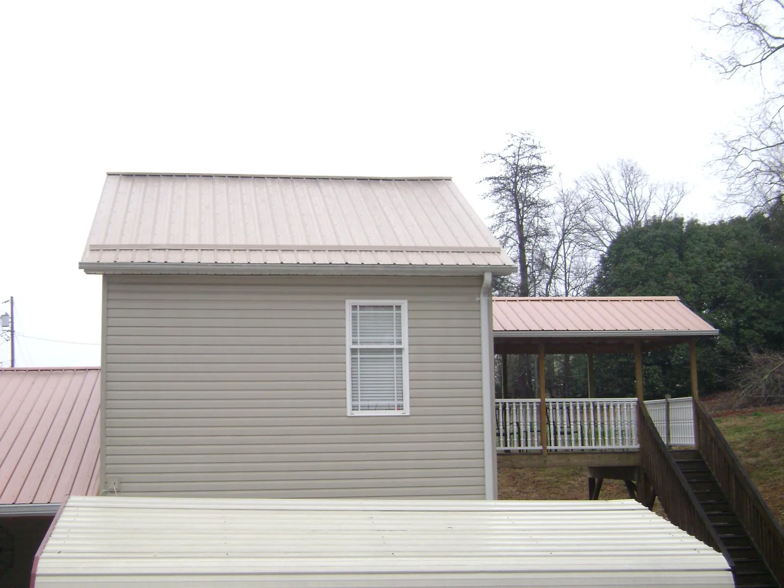 Tan metal roofs on a two story addition and attached porch, from a Roof Replacement job in Milton Center